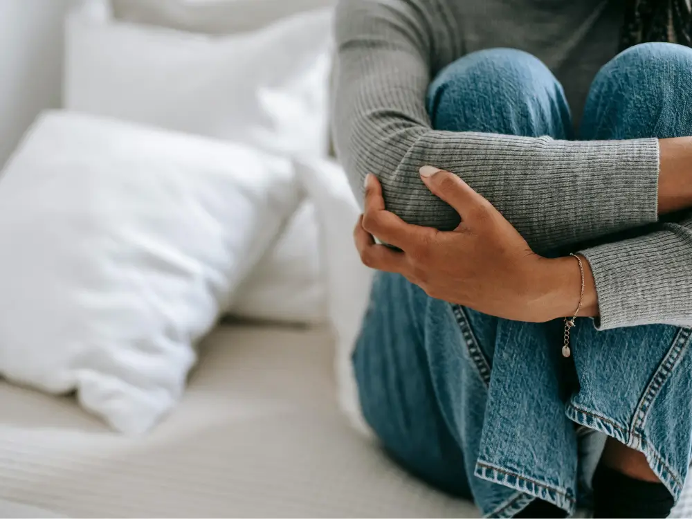 Close de uma mulher sentada, segurando o próprio braço em um gesto de autoproteção e cansaço, representando a ansiedade oculta e o peso de ser forte aos 40 anos.